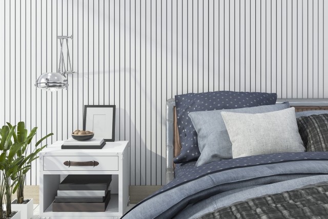a bed and side table decorated neatly in front of the bold vertical striped wallpaper