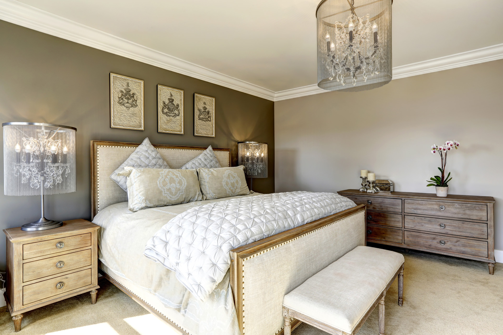 a modern decorated bedroom with a painted beige accent wall decorated with a chandelier, flowers and artwork