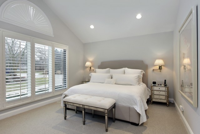 a light grey bedroom with large floor to ceiling windows covered with beautiful shutters