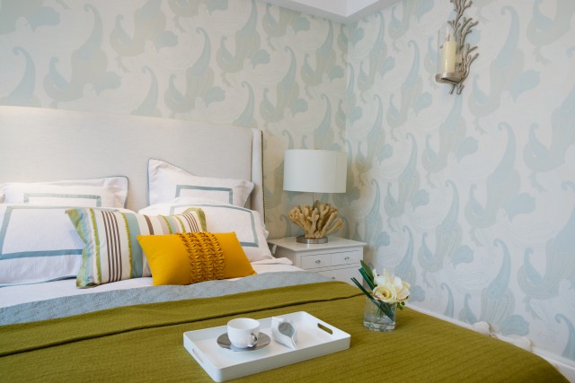 a bright decorated bed covered with throw pillows and a breakfast tray by beautiful blue wave wallpaper
